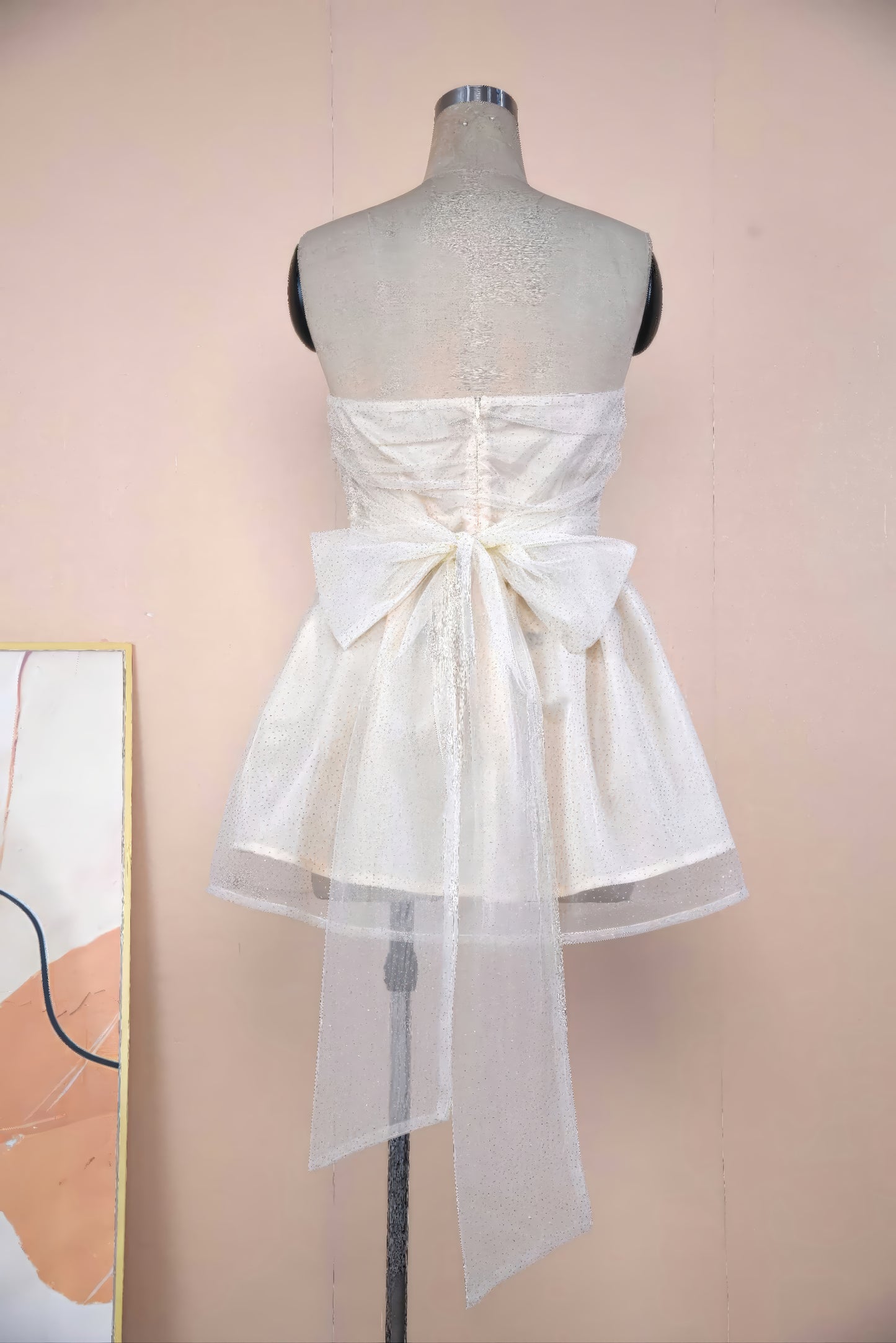 A mannequin wearing a white strapless dress with a bow detail at the back.