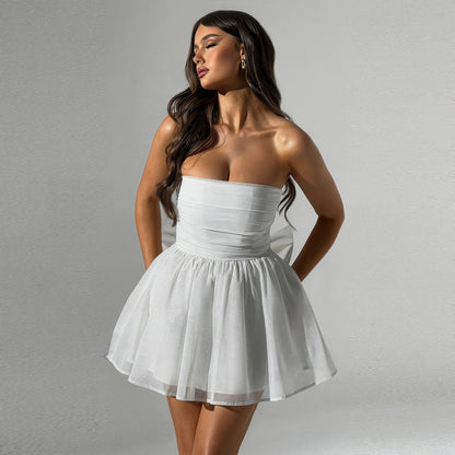 A woman wearing a strapless white dress with a full skirt, posing with her hands in her pockets against a plain background.